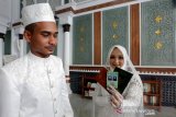 Pasangan pengantin memperlihatkan buku dan kartu nikah seusai akad di masjid Raya Baiturrahman, Banda Aceh, Aceh, Kamis (10/10/2019). Kartu nikah yang diluncurkan Kementerian Agama sejak awal November 2018 telah terhubung dalam aplikasi SIMKAH (Sistem Informasi Manajemen Nikah) guna memudahkan masyarakat dalam pengurusan dalam catatan pernikahan dan dapat dibawa sebagai tanda ikatan resmi suami istri. Antara Aceh/Irwansyah Putra.