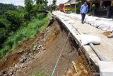 Sebuah truk melintas saat petugas memeriksa kondisi jalan rabat yang menggantung sepanjang 20 meter akibat tanah amblas terseret longsor di jalur menuju lereng Gunung Wilis, Desa Geger, Tulungagung, Jawa Timur, Selasa (17/12/2019). Plengseng jalan di jalur Selingkar Wilis itu amblas terseret longsor akibat hujan deras yang mengguyur wilayah tersebut, sehari sebelumnya. Antara Jatim/Destyan Sujarwoko/zk.