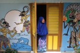 Seorang ibu membuka pintu rumahnya yang dihiasi mural wayang kulit Werkudoro di Kampung Wisata Edukasi Wayang Kulit, Samaan, Malang, Jawa Timur, Minggu (26/1/2020). Hampir seluruh dinding rumah di kampung tersebut dihias dengan mural penggalan cerita wayang kulit Mahabharata dan Ramayana untuk sarana edukasi kepada masyarakat tentang pewayangan sekaligus menghilangkan kesan kumuh. Antara Jatim/Ari Bowo Sucipto/zk