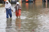 Dua orang pelajar melintasi banjir yang merendam kantor BPBD Kabupaten Indramayu, Jawa Barat, Senin (24/2/2020). Banjir tersebut akibat tingginya intensitas hujan sejak Minggu (23/2) malam, dan merendam beberapa pemukiman warga. ANTARA JABAR/Dedhez Anggara/agr