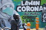 Pengendara motor berhenti di depan mural Lawan Corona di Jalan Wonokromo, Surabaya, Jawa Timur, Kamis (26/3/2020). Mural karya Serikat Mural Surabaya tersebut merupakan media edukasi kepada warga agar mencegah potensi penyebaran virus corona atau COVID-19, salah satunya dengan cara memakai masker saat beraktivitas di luar rumah. Antara Jatim/Moch Asim/zk.