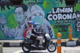 Pengendara motor melintas di depan mural Lawan Corona di Jalan Wonokromo, Surabaya, Jawa Timur, Kamis (26/3/2020). Mural karya Serikat Mural Surabaya tersebut merupakan media edukasi kepada warga agar mencegah potensi penyebaran virus corona atau COVID-19, salah satunya dengan cara memakai masker saat beraktivitas di luar rumah. Antara Jatim/Moch Asim/zk.