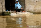 Seorang warga berada di dalam rumahnya yang digenangi banjir di Desa Pasi Leuhan, Kecamatan Johan Pahlawan, Aceh Barat, Aceh, Jumat (27/3/2020). Banjir yang disebabkan tingginya intensitas hujan dan meluapnya sungai Meureubo mengakibatkan puluhan rumah warga terendam banjir dengan ketinggian air 30 sampai 70 cm. Antara Aceh/Syifa Yulinnas.