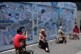Warga berjemur dengan latar belakang mural (lukisan dinding) komik antihoaks di Kampung Hepi, Joho, Manahan, Solo, Jawa Tengah, Selasa (7/4/2020). Mural tersebut dibuat warga setempat untuk mengedukasi warga tentang hidup bersih dan sehat sebagai upaya mencegah penyebaran COVID-19 sekaligus mengampanyekan gerakan antihoaks. ANTARA FOTO/Maulana Surya/nym.