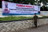 Warga melintas di dekat spanduk seruan untuk menunda mudik menjelang puasa dan lebaran di Jalan Sudirman, Serang, Banten, Kamis (9/4/2020). Pemda setempat bersama tokoh masyarakat menempuh berbagai langkah untuk memutus rantai penyebaran COVID-19 termasuk menyebar spanduk berisi seruan untuk menunda mudik. ANTARA FOTO/Asep Fathulrahman/nym.