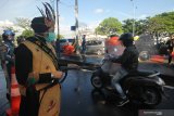 Polisi berpakaian adat menyemprotkan larutan disinfektan ke kendaraan bermotor yang memasuki Surabaya di pintu keluar Jembatan Suramadu, Surabaya, Jawa Timur, Senin (20/4/2020). Kegiatan itu untuk menghambat dan memutus penyebaran Covid-19. Antara Jatim/Didik/Zk