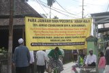 Warga melintas di dekat spanduk himbauan agar warga berdoa untuk almarhum KH Ahmad Zuhdianoor (Guru Zuhdi) di rumah saja di jalan Masuk Kediaman Guru Zuhdi di Banjarmasin, Kalimantan Selatan, Sabtu (2/5/2020). Guru Zuhdi salah satu ulama Kalimantan Selatan meninggal dunia di Rumah Sakit Medistra Jakarta. Foto Antaranews Kalsel/Bayu Pratama S.