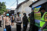 Petugas kepolisian di bantu TNI memasang poster berisi dukungan terkait isolasi mandiri di rumah warga di Waru, Jawa Timur, Minggu (17/5/2020). Warga di kawasan tersebut melakukan isolasi mandiri akibat dari salah satu warga nya di nyatakan positif COVID 19. Antara Jatim/Umarul Faruq/zk