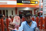 Warga menunjukan uang pembagian  Bantauan Sosial Tunai (BST) di Kantor Pos Banyuwangi, Jawa Timur, kamis (21/5/2020). Pembagian BST senilai Rp600 ribu kepada Keluarga Penerima Manfaat itu, untuk membantu meringankan beban ekonomi masyarakat saat pendemi COVID-19. Antara Jatim/Budi Candra Setya/zk