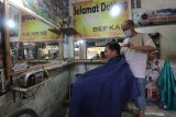 Tukang potong memangkas rambut pelanggannya di kawasan Kampung Cukur Kelurahan Kemasan, Kota Kediri, Jawa Timur, Sabtu (23/5/2020). Semenjak pandemi COVID-19 belasan tukang cukur di kawasan tersebut sepi pelanggan sehingga rata-rata penghasilan mereka menurun hingga 40 persen dan tidak ada peningkatan meskipun menjelang lebaran. Antara Jatim/Prasetia Fauzani/zk