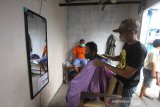 Tukang cukur menggunakan masker memangkas rambut pelanggannya di Kampung Tangguh Banua di Kelurahan Telawang Banjarmasin, Kalimantan Selatan, Rabu (17/6/2020). Warga di daerah tersebut menginisiasi kampung tangguh dengan menpersiapkan semua protokol kesehatan seperti membentuk petugas tanggap COVID-19 dan posko layanan kesehatan hingga rumah karantina khusus sebagai upaya memutus mata rantai penyebaran COVID-19. Foto Antaranews Kalsel/Bayu Pratama S.