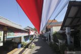 Warga melintas di kampung yang berhias kain berwarna Merah Putih di Kawasan Karangan, Surabaya, Jawa Timur, Minggu (16/8/2020). Kain berwarna Merah Putih dengan panjang sekitar 1.300 meter yang dipasang di atas jalan kampung itu untuk menyambut HUT ke-75 Kemerdekaan Republik Indonesia. Antara Jatim/Didik/Zk