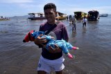 Seorang penumpang menggendong anaknya turun dari perahu di Pelabuhan Penyeberangan Antar Pulau di Likupang, Minahasa Utara, Sulawesi Utara, Senin (31/8/2020). Ketiadaan infrastruktur dermaga yang memadai mengharuskan penumpang untuk berjalan sejauh kurang lebih 60 meter menuju tepi pantai, dan menyulitkan pemilik kapal untuk bersandar saat masa pasang-surut air laut dan cuaca buruk. ANTARA FOTO/Adwit B Pramono/hp.