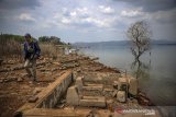 Warga melintas di samping kompleks pemakaman yang muncul kembali ke permukaan di pinggiran Waduk Jatigede, Desa Cipaku, Darmaraja, Kabupaten Sumedang, Jawa Barat, Selasa (8/9/2020). Masyarakat setempat menyatakan, musim kemarau yang telah terjadi selama dua bulan di Kabupaten Sumedang membuat debit air Waduk Jatigede menyusut hingga sekitar 5 meter dan membuat bekas permukiman serta kompleks pemakaman muncul ke permukaan. ANTARA JABAR/Raisan Al Farisi/agr