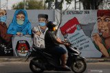 Warga melintas di dekat tembok bermural di kawasan Dupak Rukun, Surabaya, Jawa Timur, Rabu (7/10/2020). Mural tersebut sebagai bentuk sosialisasi serta ajakan kepada masyarakat untuk menggunakan hak pilihnya pada pemilihan Wali Kota dan Wakil Wali Kota Surabaya tahun 2020. Antara Jatim/Didik/Zk