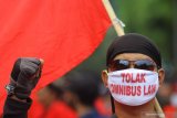 Demonstran yang tergabung dalam Gerakan Tolak Omnibus Law (GETOL) memakai masker bertuliskan Tolak Omnibus Law saat berunjuk rasa menuju Gedung Negara Grahadi di Surabaya, Jawa Timur, Selasa (20/10/2020). Unjuk rasa yang diikuti ratusan massa dari serikat pekerja dan mahasiswa dari sejumlah perguruan tinggi tersebut menolak pengesahan Undang-undang Cipta Kerja serta mendesak Presiden mencabut UU tersebut dengan menerbitkan Perppu karena dinilai merugikan rakyat khususnya para pekerja atau buruh. Antara Jatim/Moch Asim/zk.