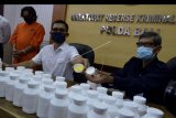 Petugas menunjukkan tersangka berinisial AMF (kiri) dan barang bukti produk obat ilegal saat rilis di Polda Bali, Denpasar, Bali, Senin (26/10/2020). Petugas Balai Besar Pengawas Obat dan Makanan (BBPOM) Denpasar bersama Ditreskrimsus Polda Bali berhasil mengamankan barang bukti sediaan farmasi yang tidak memenuhi syarat dan tanpa izin edar berupa 31.179 tablet obat yang mengandung Tiheksifenidil dan 5.172 tablet obat dengan kandungan Dextromethorpan yang akan diedarkan tersangka AMF. ANTARA FOTO/Fikri Yusuf/nym