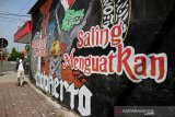 Warga melintas di depan lukisan dinding atau mural di Jalan R Wijaya Kota Mojokerto, Jawa Timur, Minggu (22/11/2020). Mural yang berpesan 