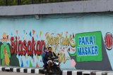 Pengendara motor melintas di dekat dinding bermural di 'Underpass' Mayjen Sungkono, Surabaya, Jawa Timur, Minggu (22/11/2020). Mural di dinding 'Underpass' Mayjen Sungkono tersebut merupakan sarana imbauan kepada warga untuk tetap menerapkan protokol kesehatan pencegahan penularan COVID-19. Antara Jatim/Didik/Zk