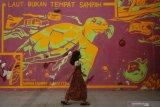 Seorang anak melintas di depan mural dengan tulisan 