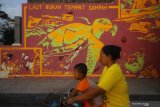 Warga melintas di depan mural dengan tulisan 