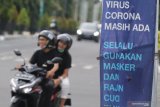 Pengedara sepeda motor tanpa menggunakan masker melintas di dekat sepanduk sosialisasi penerapan protokol kesehatan di Kota Kediri, Jawa Timur, Jumat (25/12/2020). Kedisiplinan masyarakat menerapkan protokol kesehatan di wilayah tersebut masih kurang meskipun pemerintah telah berupaya mensosialisasikan penanggulangan penyebaran COVID-19. Antara Jatim/Prasetia Fauzani/Um