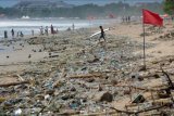 Wisatawan berjalan melewati sampah kiriman yang terdampar memenuhi pesisir Pantai Kuta, Badung, Bali, Kamis (31/12/2020). Jelang pergantian tahun baru, obyek wisata Pantai Kuta tampak sepi menyusul adanya aturan larangan pesta perayaan pergantian tahun baru dan pemberlakuan jam malam untuk pengendalian aktivitas masyarakat yang dibatasi hingga pukul 23.00 WITA. ANTARA FOTO/Nyoman Hendra Wibowo/nym.