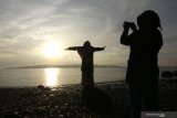 Warga berfoto dengan latar belakang matahari terbit di Watudodol ,Banyuwangi, Jawa Timur, Jumat (1/1/2021). Kabupaten Banyuwangi yang terletak di ujung timur pulau Jawa itu menjadi salah satu tempat favorit untuk menyaksikan matahari terbit pertama kali di awal tahun 2021. Antara Jatim/Budi Candra Setya/zk