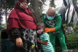 Tokoh 'New Man' memakaikan masker kepada anak saat melakukan imbauan protokol kesehatan di Kebun Binatang Surabaya, Jawa Timur, Jumat (1/1/2021). Kegiatan imbauan protokol kesehatan yaitu Memakai Masker, Menjaga Jarak, Mencuci Tangan itu bertujuan agar masyarakat tetap terus menerapkan protokol kesehatan pencegahan penyebaran COVID-19 dalam kesehariannya. Antara Jatim/Didik/Zk