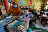 Guru membagikan buku pelajaran kepada pelajar pada hari pertama sekolah tatap muka di SD Negeri 42, Banda Aceh, Aceh, Senin (4/1/2021). Mayoritas lembaga pendidikan tingkat SD, SMP dan SMA di provinsi Aceh mulai melaksanakan pembelajaran tatap muka dengan sistim bergiliran dan menerapkan protokol kesehatan secara ketat untuk mencegah penularan COVID-19. Antara Aceh/Irwansyah Putra.