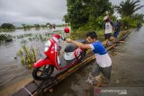 Warga membantu pengendara melintasi titian kayu swadaya masyarakat untuk membantu pengendara roda dua di jalan Martapura Lama yang terendam banjir akibat luapan Sungai Martapura di Kabupaten Banjar, Kalimantan Selatan, Kamis (7/1/2021).Menurut warga setempat, banjir akibat luapan Sungai Martapura sudah berlangsung selama 15 hari merendam kawasan tersebut sehingga mengganggu aktivitas warga, dan hingga Kamis (7/1/2021) pemerintah daerah belum memberikan bantuan apapun. Foto Antaranews Kalsel/Bayu Pratama S.