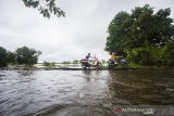 Warga membantu pengendara melintasi titian kayu swadaya masyarakat untuk membantu pengendara roda dua di jalan Martapura Lama yang terendam banjir akibat luapan Sungai Martapura di Kabupaten Banjar, Kalimantan Selatan, Kamis (7/1/2021). Menurut warga setempat, banjir akibat luapan Sungai Martapura sudah berlangsung selama 15 hari merendam kawasan tersebut sehingga mengganggu aktivitas warga, dan hingga Kamis (7/1/2021) pemerintah daerah belum memberikan bantuan apapun. Foto Antaranews Kalsel/Bayu Pratama S.