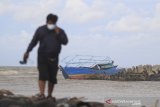 Seorang warga berada di sekitar kapal nelayan pencari cumi yang karam di sekitar muara Eretan wetan, Kandanghaur, Indramayu, Jawa Barat, Rabu (13/1/2021). Kapal Cumi tersebut karam akibat diterjang gelombang tinggi saat akan memasuki muara. ANTARA JABAR/Dedhez Anggara/agr