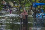 Warga menuntun sepedanya melintasi banjir yang merendam Jalan Prona di Banjarmasin, Kalimantan Selatan, Kamis (14/1/2021). Tingginya intensitas curah hujan mengakibatkan sejumlah kawasan di Kota Banjarmasin terendam banjir. Foto Antaranews Kalsel/Bayu Pratama S.