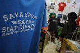 Pekerja menyelesaikan pembuatan kaos dengan tulisan siap divaksin di toko kaos 