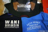 Pekerja menyelesaikan pembuatan kaos dengan tulisan siap divaksin di toko kaos 