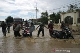 Warga membantu pengendara motor saat melintasi banjir di Jalan nasional Surabaya-Madiun Desa Gondangmanis, Kecamatan Bandar Kedungmulyo Kabupaten Jombang, Jawa Timur, tergenang banjir, Kamis (4/2/2021). Banjir yang disebabkan meluapnya sungai avur Brawijaya di desa setempat mengakibatkan kemacetan kendaraan mengular hingga 1 kilometer, selain itu juga menggenangi puluhan rumah serta warung makan. Antara Jatim/Syaiful Arif/zk.