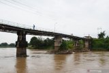 Warga melintas di atas jembatan yang salah satu pilarnya ambles di Sungai Madiun, Kota Madiun, Jawa Timur, Jumat (5/2/2021). Menurut warga amblesnya pilar jembatan tersebut akibat derasnya arus sungai selama dua hari terakhir, dan warga sekitar menutup akses jembatan untuk semua jenis kendaraan guna menghindari terjadinya musibah. Antara Jatim/Siswowidodo/zk.