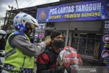 Petugas kepolisian memakaikan masker kepada seorang pengendara saat operasi kepatuhan memakai masker di Posko Lantas Tangguh, Cileunyi, Kabupaten Bandung, Jawa Barat, Rabu (10/2/2021). Polresta Bandung membagikan masker dan menggelar operasi kepatuhan dalam pelaksanaan PPKM berskala mikro yang merupakan perpanjangan dari PPKM Jawa-Bali guna mendorong Kabupaten Bandung menjadi zona hijau COVID-19, yang digelar hingga 26 Februari 2021. ANTARA JABAR/Raisan Al Farisi/agr