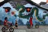 Dua anak bermain di dekat mural Naga di kampung Pecinan di Kapasan Dalam, Surabaya, Jawa Timur, Kamis (11/2/2021). Mural itu guna memperindah salah satu kampung Pecinan tertua di Surabaya tersebut. Antara Jatim/Didik/Zk