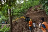 Pekerja menggunakan alat berat membersihkan reruntuhan tanah longsor dari tebing yang menimbun jalan di Desa Ngranget, Dagangan, Kabupaten Madiun, Jawa Timur, Jumat (2/4/2021). Tebing di lembah Gunung Wilis tersebut longsor akibat hujan deras Kamis (1/4) malam. Antara Jatim/Siswowidodo/zk.