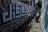 Warga melintas di depan mural kaligrafi di Kampung Wisata Budaya Kaligrafi di Bandung, Jawa Barat, Jumat (16/4/2021). Warga di kawasan tersebut berswadaya untuk membuat mural kaligrafi dan menghias tembok dengan potongan hadits, ayat Al Quran hingga Asmaul Husna untuk memberikan susana kampung yang unik namun tetap bernuansa Islami bagi masyarakat sekitar ataupun pendatang. ANTARA JABAR/Novrian Arbi/agr