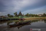 Sebuah perahu bermesin melintas di Sungai Kuin dengan latar belakang Masjid Sultan Suriansyah di Banjarmasin, Kalimantan Selatan, Senin (19/4/2021). Masjid Sultan Suriansyah atau Masjid Kuin merupakan bangunan masjid tertua di Kalsel yang memiliki bentuk arsitektur tradisional Banjar dengan konstruksi panggung dan beratap tumpang yang dibangun pada masa pemerintahan Sultan Suriansyah (1526 Masehi-1550 Masehi). Foto Antaranews Kalsel/Bayu Pratama S.