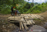 Pengendara motor melintasi jembatan yang rusak di Desa Hinas Kanan, Kabupaten Hulu Sungai Tengah, Kalimantan Selatan, Senin (5/7/2021). Warga setempat mengeluhkan jalan penghubung antar desa yang berada di Kecamatan Hantakan tersebut masih rusak parah akibat longsor pascabanjir bandang dan hingga kini belum diperbaiki sehingga mengganggu aktivitas warga. Foto Antaranews Kalsel/Bayu Pratama S.