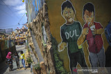 Sejumlah anak bermain di samping dinding yang dihias oleh mural yang bertemekan keagamaan di Kampung Kukun Endah, Desa Cikoneng, Kabupaten Bandung, Jawa Barat, Kamis (26/1/2021). Warga berinisiatif untuk menghias dinding dengan tema keagaaman guna memberikan edukasi pada anak tentang ilmu keagamaan serta menjaga dinding dari coretan vandalisme. ANTARA FOTO/Raisan Al Farisi/agr