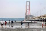 Warga melintas di bawah jembatan Suramadu Surabaya, Jawa Timur, Minggu (3/10/2021). Kawasan tersebut menjadi wisata alternatif bagi masyarakat sekitar saat tempat wisata di Surabaya belum dibuka. Antara Jatim/Umarul Faruq/zk.