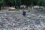  Warga melintas di antara sampah yang berada di pantai pelabuhan Muncar, Banyuwangi, Jawa Timur, Selasa (9/11/2021). Sampah plastik dan tekstil yang terbawa air laut itu menumpuk di pantai sehingga menjadi masalah lingkungan yang bertahun-tahun belum teratasi. Antara Jatim/Budi Candra Setya/zk