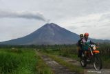 Dua orang relawan melintas dengan latar Gunung Semeru mengeluarkan  Awan Panas Guguran (APG) melalui bukaan aliran lava baru Gunung Semeru terlihat dari desa Supiturang, Pronojiwo, Lumajang, Jawa Timur, Selasa (21/12/2021). Pusat Riset Aplikasi Penginderaan Jauh Lapan - Badan Riset dan Inovasi Nasional (BRIN) mencatat gunung Semeru mengalami perubahan bentuk di wilayah kawah hingga lereng di bagian tenggara akibat aktivitas vulkanik berupa luncuran awan panas guguran. Antara Jatim/Ari Bowo Sucipto/zk