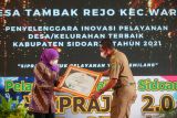 Gubernur Jawa Timur Khofifah Indar Parawansa (kiri) memberikan secara simbolis penghargaan kepada penyelenggara inovasi pelayanan Desa/Kecamatan terbaik saat peluncuran Sistem Pelayanan Rakyat Sidoarjo (SIPRAJA) di Pendopo Sidoarjo, Jawa Timur, Selasa (28/12/2021). Pemkab Sidoarjo meluncurkan Sistem Pelayanan Rakyat Sidoarjo (SIPRAJA 2.0) yang bertujuan untuk memberikan pelayanan prima, cepat, mudah, transparan serta berkualitas kepada masyarakat dalam mengurus 22 jenis pelayanan. Antara Jatim/Umarul Faruq/zk