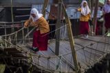 Sejumlah murid SD melintasi jembatan gantung yang rusak di Desa Tanipah, Kabupaten Banjar, Kalimantan Selatan, Rabu (10/11/2021). Meski membahayakan keselamatan, warga setempat masih menggunakan jembatan gantung yang rusak akibat diterjang arus luapan sungai tersebut untuk beraktivitas. ANTARA FOTO/Bayu Pratama S/WSJ.